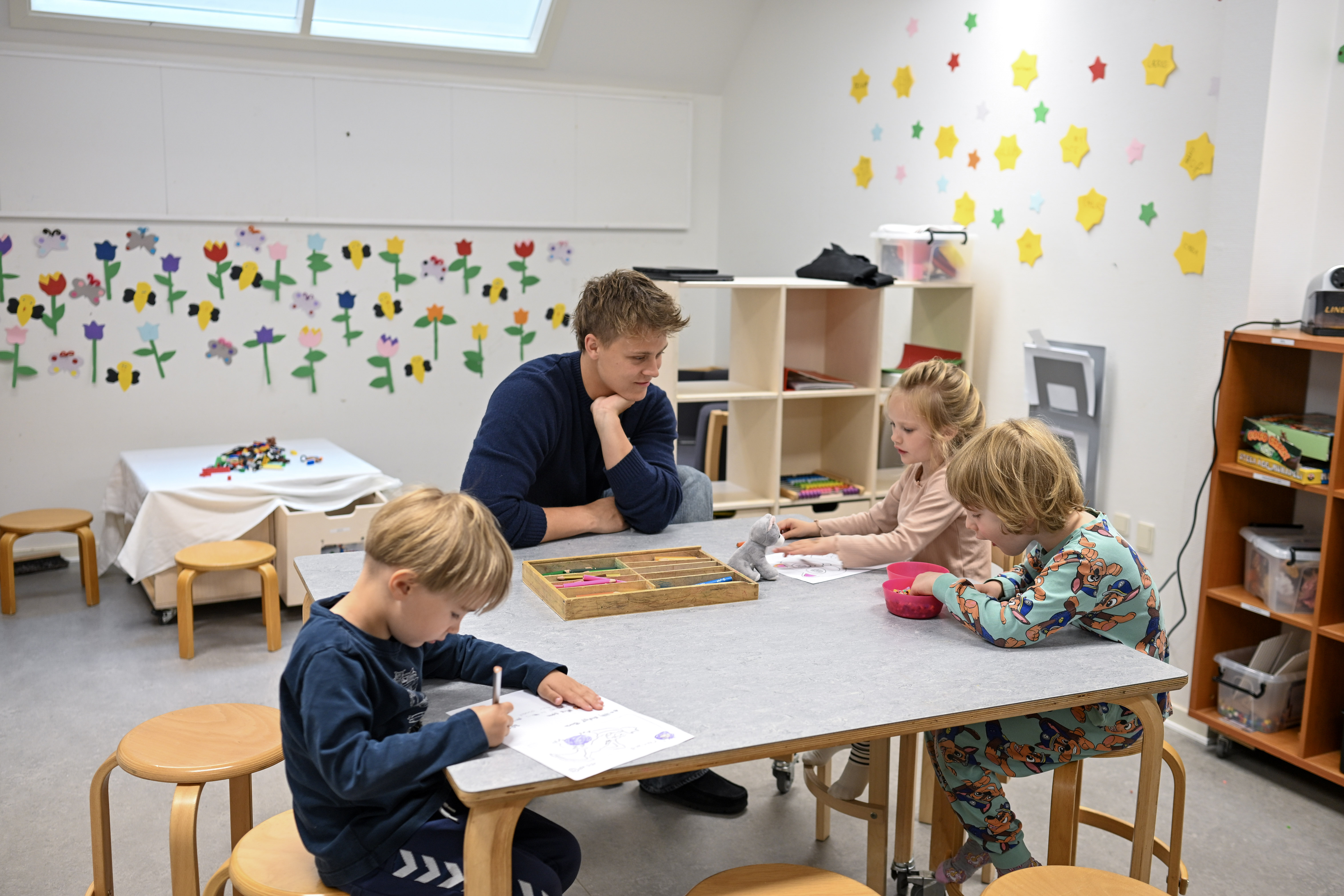 Børn er kreative ved et bord, mens en voksen kigger på